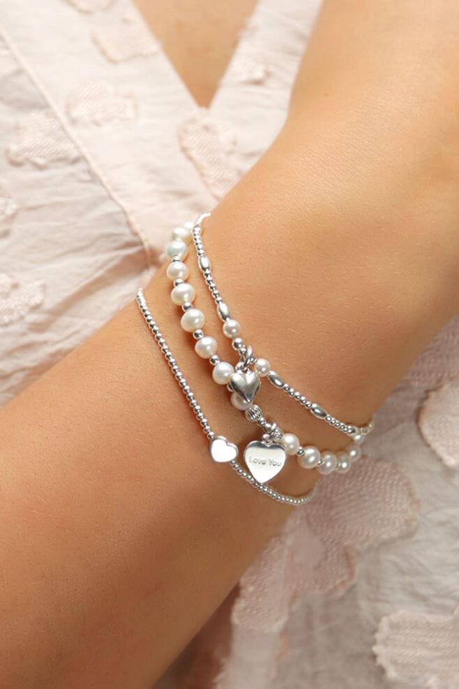 Bracelet stack made up of three strands, featuring pearls, silver beads and an engraved heart charm.