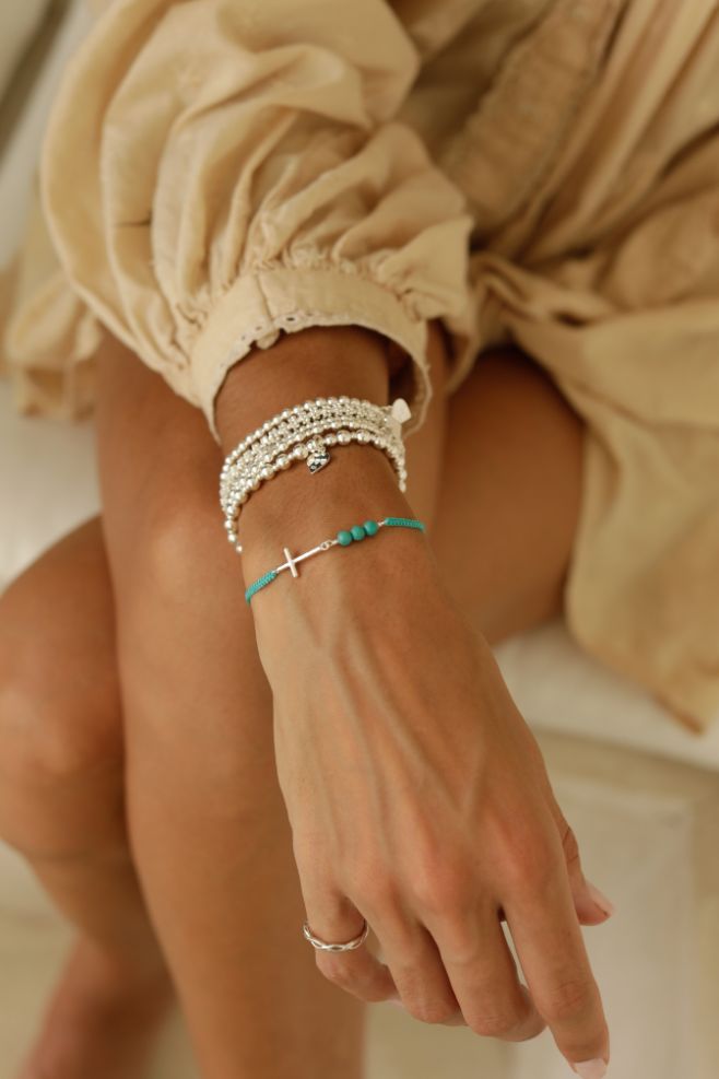 A fun 925 Sterling Silver bracelet that features a solid sideways cross charm and turquoise magnesite beads.
