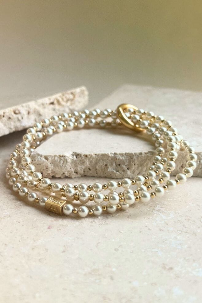 A chic wrap style bracelet featuring a continuous unbroken yard of Preciosa Pearls and dainty gold plated silver beads held together with an iconic binding ring and finished off with an engraved Pearls of Wisdom bead.