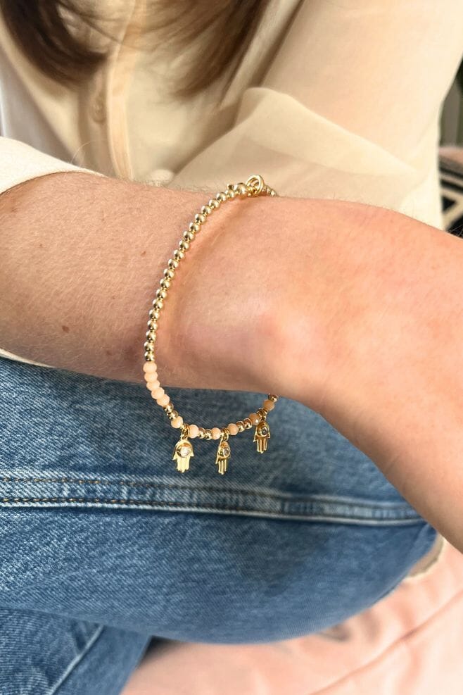 A dainty gold plated Silver and peach glass Annie Haak beaded bracelet in a stylish design, featuring three Fatima’s Hand charms with a moonstone feature for protection, luck, and harmony.