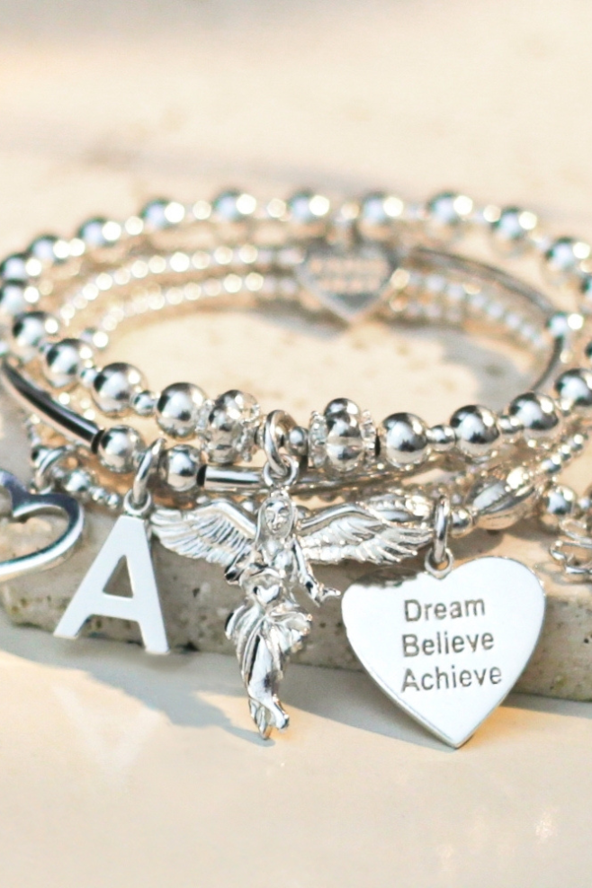 Personalised sterling silver bracelet stack featuring five beaded bracelets with a guardian angel charm, engraved initial disc, four-heart clover and open heart charms.
